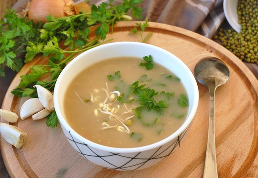 Healthy vegan soup from mung bean, coriander, garlic and onion in bowl on wooden background