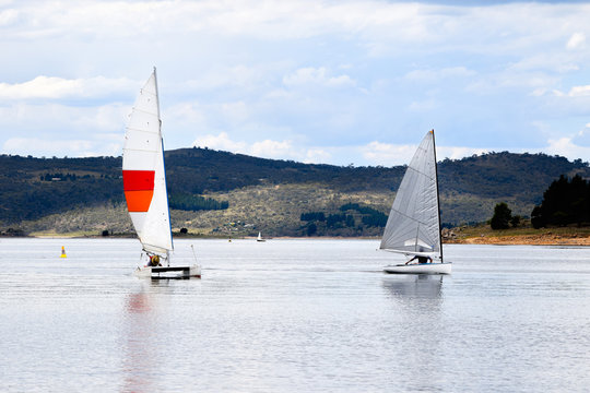 Two sail boats during a local race on a lake at the foothills of a mountain range
