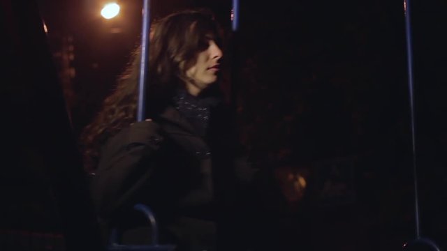 Sad lonely girl riding at night on a swing in the park with city lights