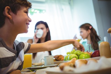 Boy picking up fruits from tray while having breakfast