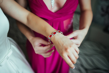 Obraz na płótnie Canvas Girl wears a bracelet on a hand of the bride, bride's morning, preparing for the wedding, the bride's fees, dress, decorate the bride, wedding attributes, jewelery, bracelet bride dress