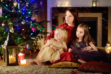 Young mother and her two daughters unwrapping Christmas gifts by a fireplace