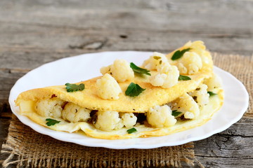 Stuffed omelet with cauliflower and parsley on an old wooden table. Vegetarian breakfast. Rustic style