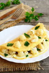 Omelet stuffed with cauliflower and parsley on a plate, fork, knife, burlap on an old wooden table. Diet breakfast recipe. Vintage style