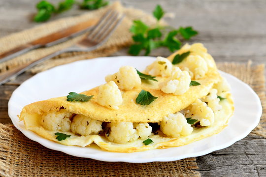 Stuffed omelet with cauliflower and parsley, fork, knife, burlap on an old wooden table. Vegetarian breakfast recipe. Rustic style