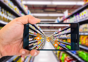 Augmented reality application for retail business concept. Hand holding smart phone with A/R application on screen to scanning sale alert in supermarket.