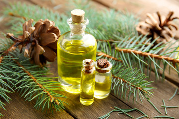 Bottles of coniferous essential oil, branches and strobiles on wooden background, close up view