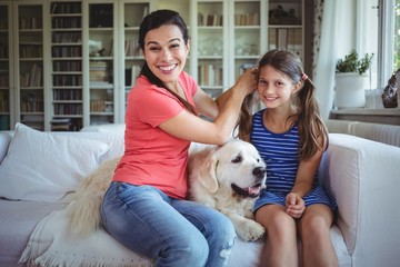 Mother sitting on sofa and tying daughters hair in living room