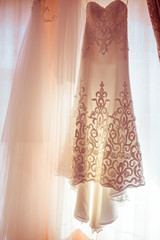 Sun shines through the wedding dress hanging on the window