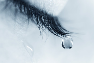Sad woman concept - closed eyelid closeup with a teardrop on eyelashes.  A tear on eyelashes macro close-up. A tear runs down his cheek. Tinted blue. - obrazy, fototapety, plakaty
