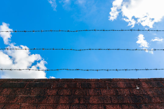 Looking up sky through barbed wire and red brick wall