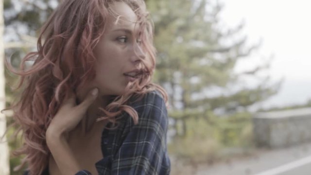 Sensual girl hipster with pink hair wearing a knit bra and shirt walking on the road in a mountainous area with forest