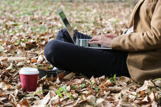 Young woman sitting in park with laptop and coffee