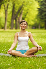 Happy young woman sitting outdoors in yoga position