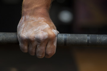 Closeup of male hand with powder holding barbell.