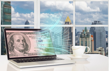 FINTEC concept image. Laptop computer with US bank note and digital code abstract on its screen against the city outside building background.