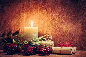 Chistmas presents, gifts with a candle glowing on wooden wall background.