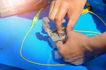 Technician using cleaver cutting optic fiber on blue table with