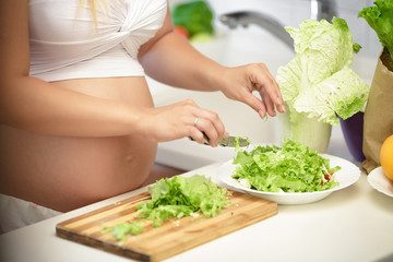 pregnant woman cuts lettuce on wooden Board