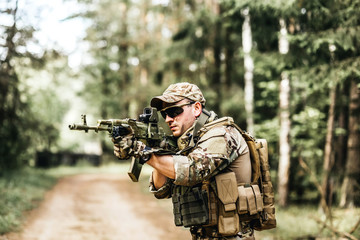 Fototapeta premium military. Armed young man in a zone of armed conflict soldier in uniform targeting with assault rifle outdoors, airsoft