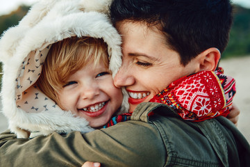 Closeup group portrait of white Caucasian mother and daughter baby girl hugging smiling laughing on sunset, autumn fall winter season, happy lifestyle childhood concept