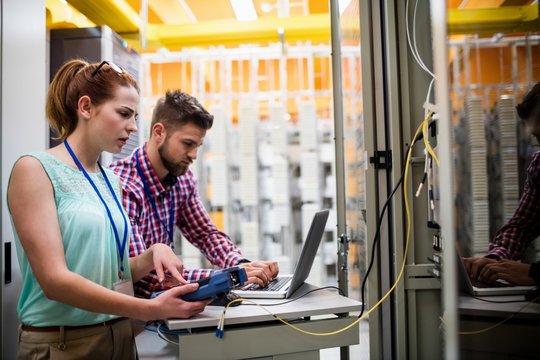 Technicians using laptop while analyzing server - Powered by Adobe