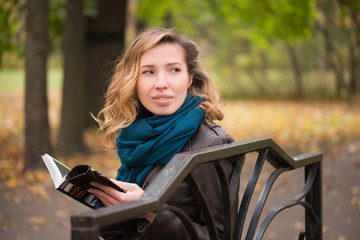 Beautiful girl blonde with wavy hair sitting on a park bench and reading a book