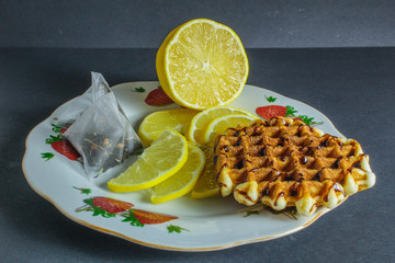 Viennese waffles topped with chocolate and sliced lemon in a plate on dark background