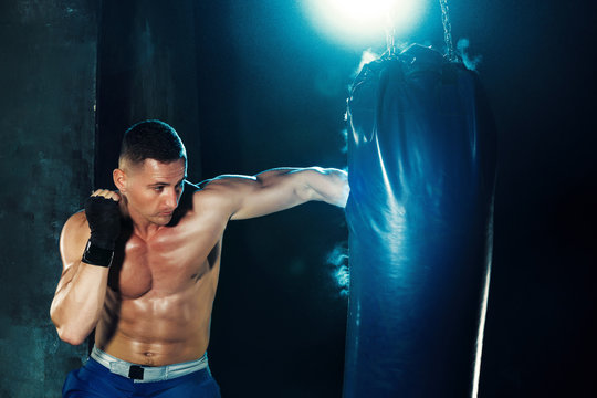 Male boxer boxing in punching bag with dramatic edgy lighting in a dark studio