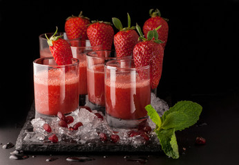 a few glasses of drink with strawberry and ice on a black stone on a dark background