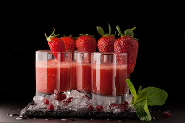 a few glasses of drink with strawberry and ice on a black stone on a dark background