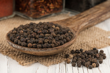 Black peppercorns in a wooden spoon and old wooden table.