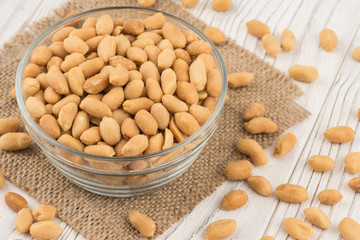 Salted peanuts in a glass bowl on the old wooden table.