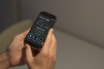 Hands holding mobile phone with connected car app on the screen. All screen graphics are made up.