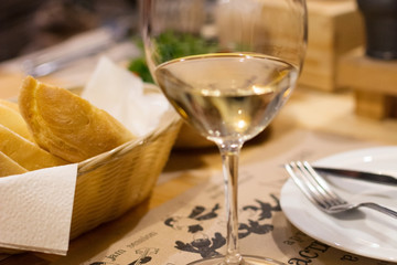 white bread in a basket, a glass of white wine on a table in a c