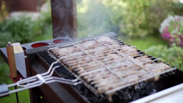 Man grilling pork meat on brazier, flipping pieces.