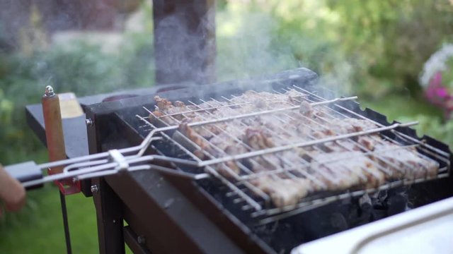 Man grilling pork meat on brazier, flipping pieces.