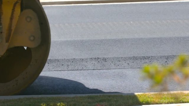 Steam Off Pavement After Roller Smooths. A close up shot of a pavement roller vehicle drives left in slow motion smoothing asphalt on a newly paved road
