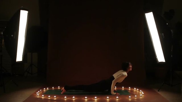 Young caucasian woman doing yoga exercise in the light of candles