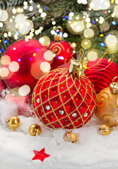 red and gold christmas ball in snow under fir evergreen tree with lights bokeh