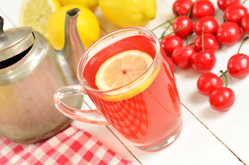 Fruit cherry tea with slice of lemon in mug, old teapot and cherries