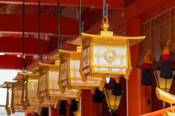 Kyoto, Japan - September 17, 2016: Fushimi Inari Taisha Shinto Shrine. Closeup of a line of golden lanterns hanging off the vermilion ceiling in front of the idols.