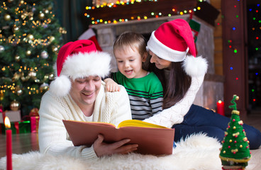 Fototapeta na wymiar Happy family of three reading book together on Christmas evening