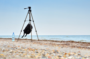 Photographic tripod is on the beach blue sea. Seascapes and photographic equipment.