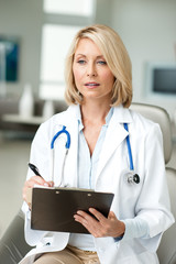 Blond Woman Doctor Taking Notes in Office with Clipboard