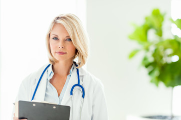 Attractive blond female woman doctor nurse practitioner in hospital clinic medical center office with clipboard