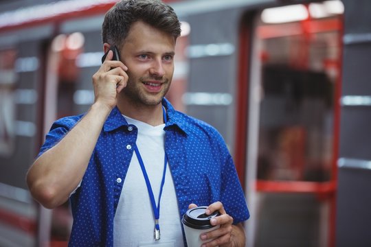 Handsome holding disposable cup while talking on mobile phone