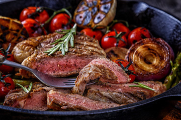 Steak with grilled vegetables in a frying pan.