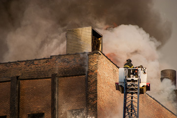 Firefighters spraying water into burning building smoke billowing out of roof downtown Chicago