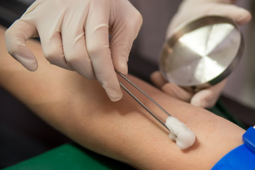 A doctor disinfects the forearm of a patient before performing a venipuncture. Healthcare and...